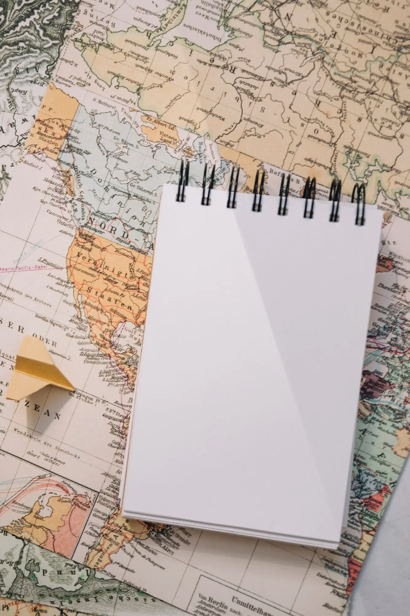 Nahaufnahme eines Notizbuchs und eines Papierflugzeugs auf einer Karte.